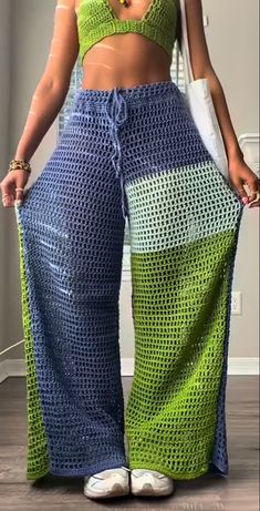 a woman in a green and blue crochet top is standing with her hands on her hips