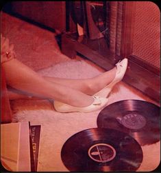 a woman's legs in high heels next to various records on the floor,