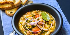 a black bowl filled with beans and veggies next to slices of bread on a blue napkin