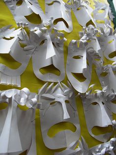 white paper cut out into masks on a yellow tablecloth with ribbons and flowers around them