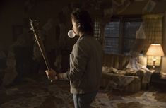 a man standing in a living room holding a baseball bat and blowing bubbles into his mouth