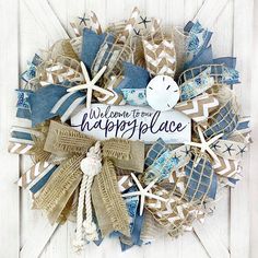 a welcome to our happy place wreath on a white wooden door with blue and tan burlocks