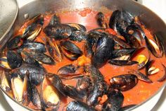 a pan filled with mussels and sauce on top of a stove