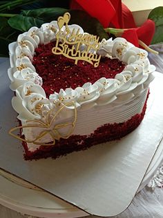 a heart shaped red velvet cake with white frosting and gold decorations on top, sitting on a plate