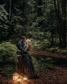 a couple standing next to each other in the woods surrounded by trees with candles on them