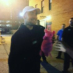 a man holding a pink stuffed animal in his right hand and smiling at the camera