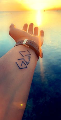 a person's arm with a wrist tattoo on it and the sun in the background