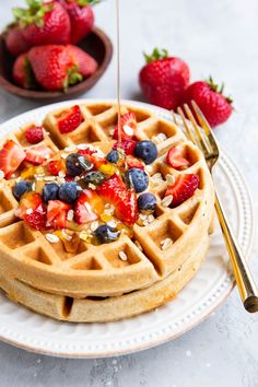 a waffle topped with strawberries and blueberries being drizzled with syrup