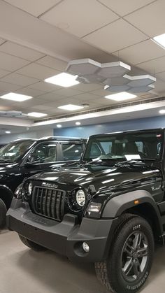 two black jeeps are parked in a garage with lights on the ceiling above them