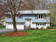 a blue house in the middle of a green yard with trees and grass around it