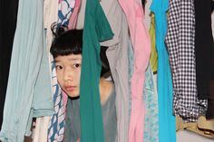 a young boy is peeking out from behind a closet full of clothes and scarves