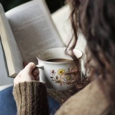 a woman reading a book and holding a cup of coffee