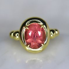 This one-of-a-kind statement ring features a vibrant orange-pink tourmaline as its centerpiece. Set in 14K yellow gold, the tourmaline is encircled by a chunky golden bezel a unique bubble-like design on the side of the band. This custom-designed ring is perfect for adding a pop of color to any outfit and making a bold fashion statement. The orange-pink tourmaline is a rare and unique gemstone and the yellow gold band gives the ring a warm and elegant look. The ring is unique and has a special d Yellow Gold Ruby Ring With Tourmaline Center Stone, Unique Pink Tourmaline Rings, Oval Pink Tourmaline Ruby Ring, Candy Ring, Pink Engagement, Spinel Jewelry, Pink Engagement Ring, Red Tourmaline, Rubellite Tourmaline