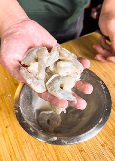 a person holding something in their hand over a metal bowl on top of a wooden table