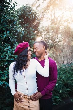 a man and woman standing next to each other in front of some bushes with the sun shining on them