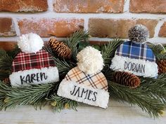 three knitted hats with personalized names and pine cones are sitting in front of a brick wall