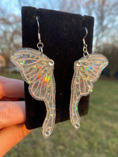 a pair of butterfly shaped earrings sitting on top of a black velvet stand in front of a grass field