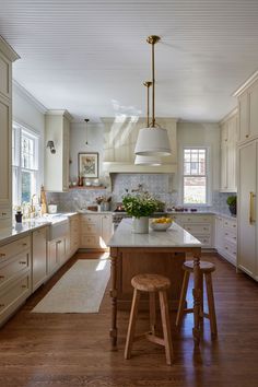 a large kitchen with white cabinets and wooden stools in the center island, along with an area rug that matches the hardwood flooring