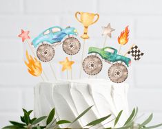 a birthday cake with monster trucks and stars on top, sitting in front of a white brick wall