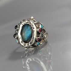 Sterling Silver Statement Ring, Labradorite Ring, Gemstone Ring, Labradorite Queen Ring, Multistone Ring, Statement Jewelry, Gift for HerThis statement labradorite ring, in an antique style, is unique and will make you feel like a real queen on your special day! At the center, you will find an enchanting labradorite gemstone on sterling silver bezel.The silver is hammered around the labradorite and makes this ring a true and delightful organic piece.Small garnet and turquoise gemstones on both s Fusion Rings With Oval Natural Stones, Fusion Oval Rings With Natural Stones, Fusion Style Oval Ring With Natural Stones, Fusion Style Oval Rings With Natural Stones, Artisan Labradorite Gemstone Rings, Artisan Moonstone Ring With Natural Stones, Unique Labradorite Rings With Natural Stones, Rose Engagement Ring Vintage, Gold Antique Engagement Rings