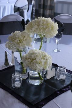 three vases filled with white flowers sitting on top of a black tablecloth covered table