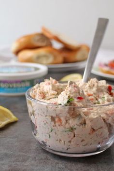 a glass bowl filled with tuna salad next to lemon wedges and baguettes