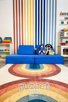 a blue couch sitting on top of a rug in front of a rainbow colored wall