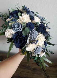 a bridal bouquet with blue and white flowers is being held by someone's hand