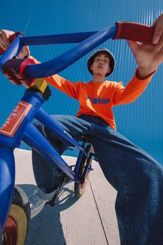 a boy in an orange shirt is sitting on a blue bike