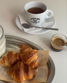 three croissants on a plate next to a cup of coffee and milk