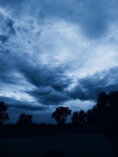 the sky is very dark and cloudy with some clouds in it, as well as trees