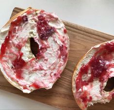 two bagels with cream cheese and strawberry toppings on a cutting board next to each other