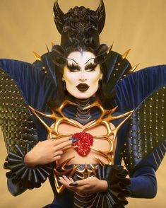 a woman dressed in blue and gold with horns on her head holding a red heart