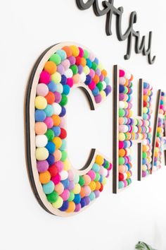 the colorful letters are made out of pom - poms and hanging on the wall