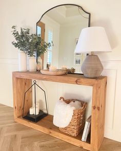 a wooden shelf with a mirror, basket and candle holder on it in front of a white wall