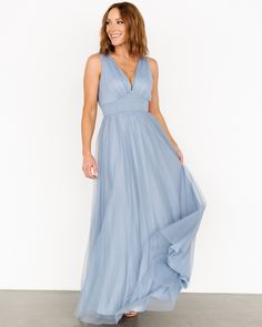 a woman in a long blue dress is smiling and looking at the camera with her hands on her hips