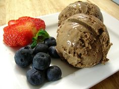 two scoops of chocolate ice cream and berries on a white plate with a strawberry