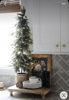 a small christmas tree in the corner of a kitchen with plates and cups on it