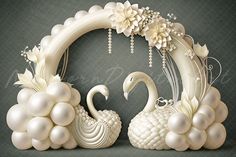 two white swans sitting on top of each other in front of a circular frame with flowers and pearls