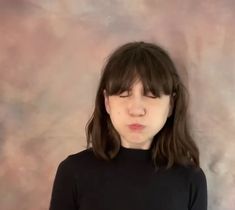 a woman with long hair and bangs standing in front of a wall