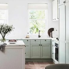 a kitchen with green cabinets and white counter tops, an island in the middle has flowers on it