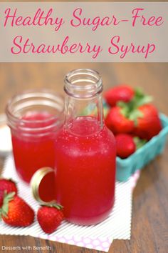 two jars filled with liquid sitting on top of a wooden table next to strawberries