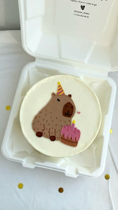 a cake shaped like a cow with a birthday hat on it in a white box