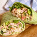 a wrap filled with meat and lettuce on top of a wooden cutting board