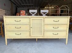 a yellow dresser with six drawers and two chairs in the back ground next to each other