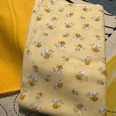 two pieces of yellow fabric with bees and flowers on them, sitting next to each other