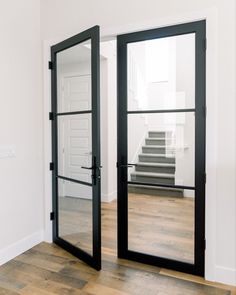 an empty room with two black doors and stairs in the background, looking into another room