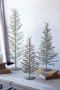 three small pine trees sitting on top of a table next to books and a candle