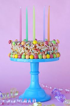 a birthday cake with candy and candles on a blue pedestal surrounded by streamers, confetti and beads