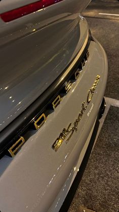 the back end of a white car with gold emblems on it's hood